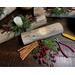 A Christmas yule log candle centerpiece. It is made from upcycled wood with a white candle, greenery, and berries arranged on the top.  